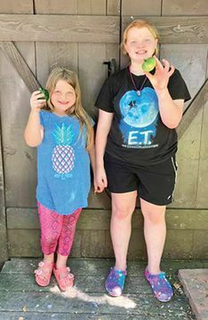 Summer Moore and Brooklyn Wallace with a pepper and 
a green tomato from their garden.